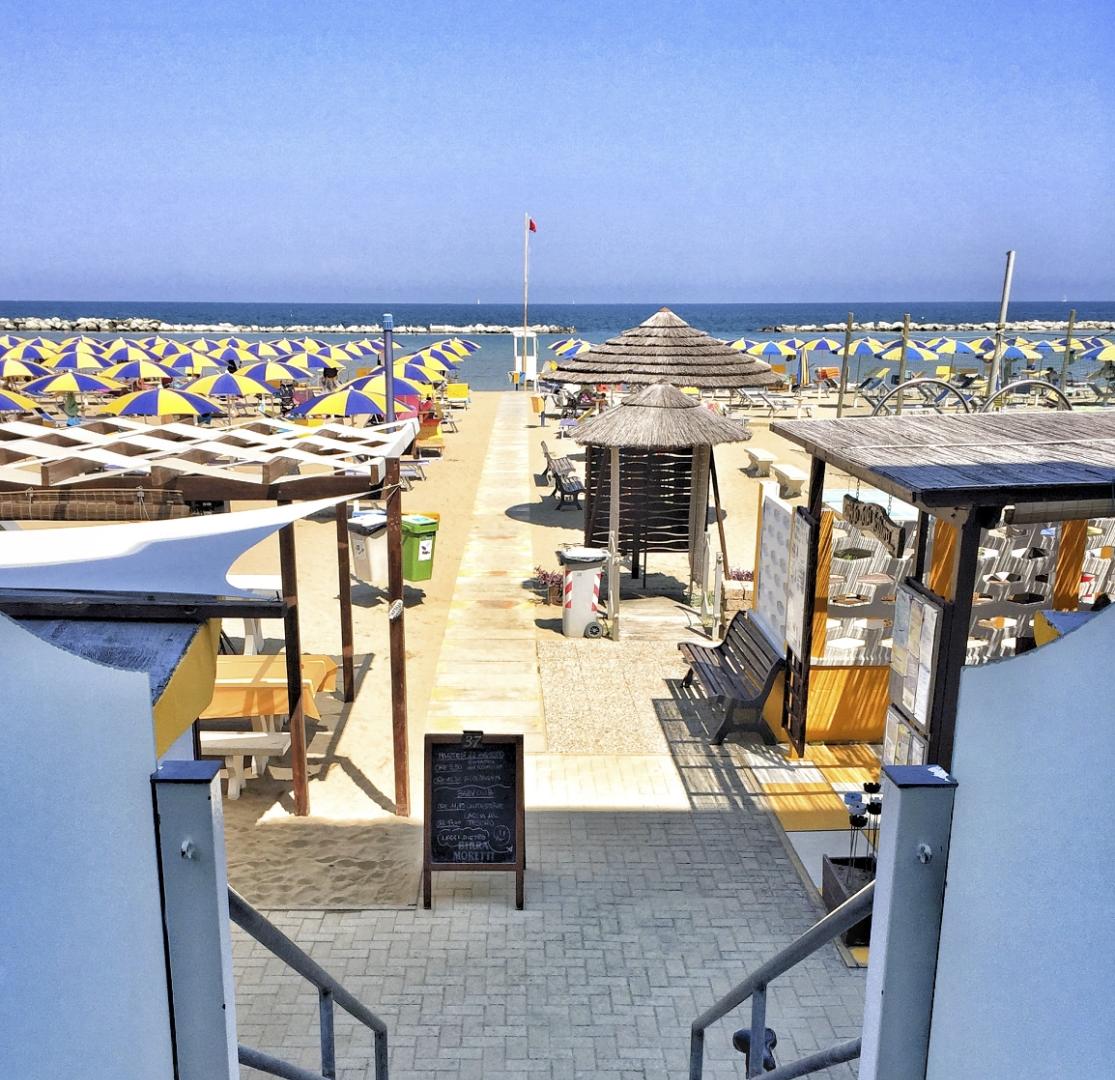 Spiaggia con ombrelloni colorati, passerella verso il mare e strutture in legno.