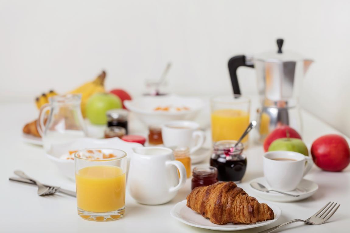 Colazione con croissant, succo d'arancia, caffè e frutta su un tavolo bianco.