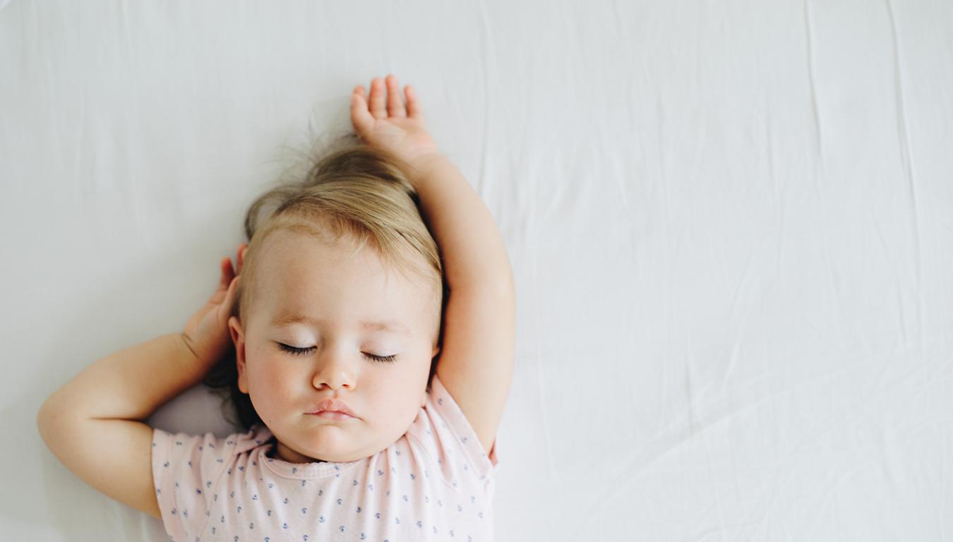 Bambino che dorme serenamente su un letto con braccia alzate.