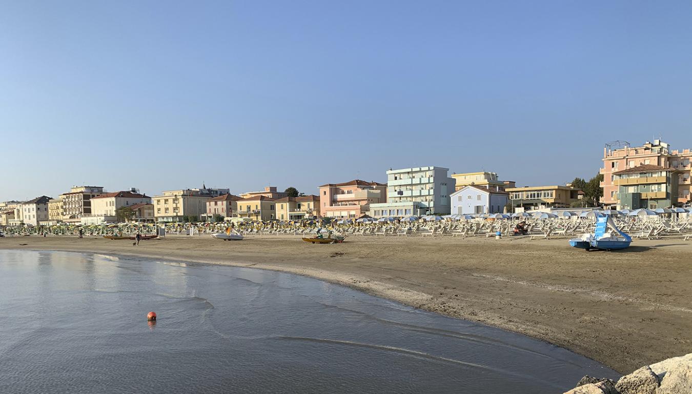 Spiaggia con ombrelloni e edifici sullo sfondo, vista da una scogliera.