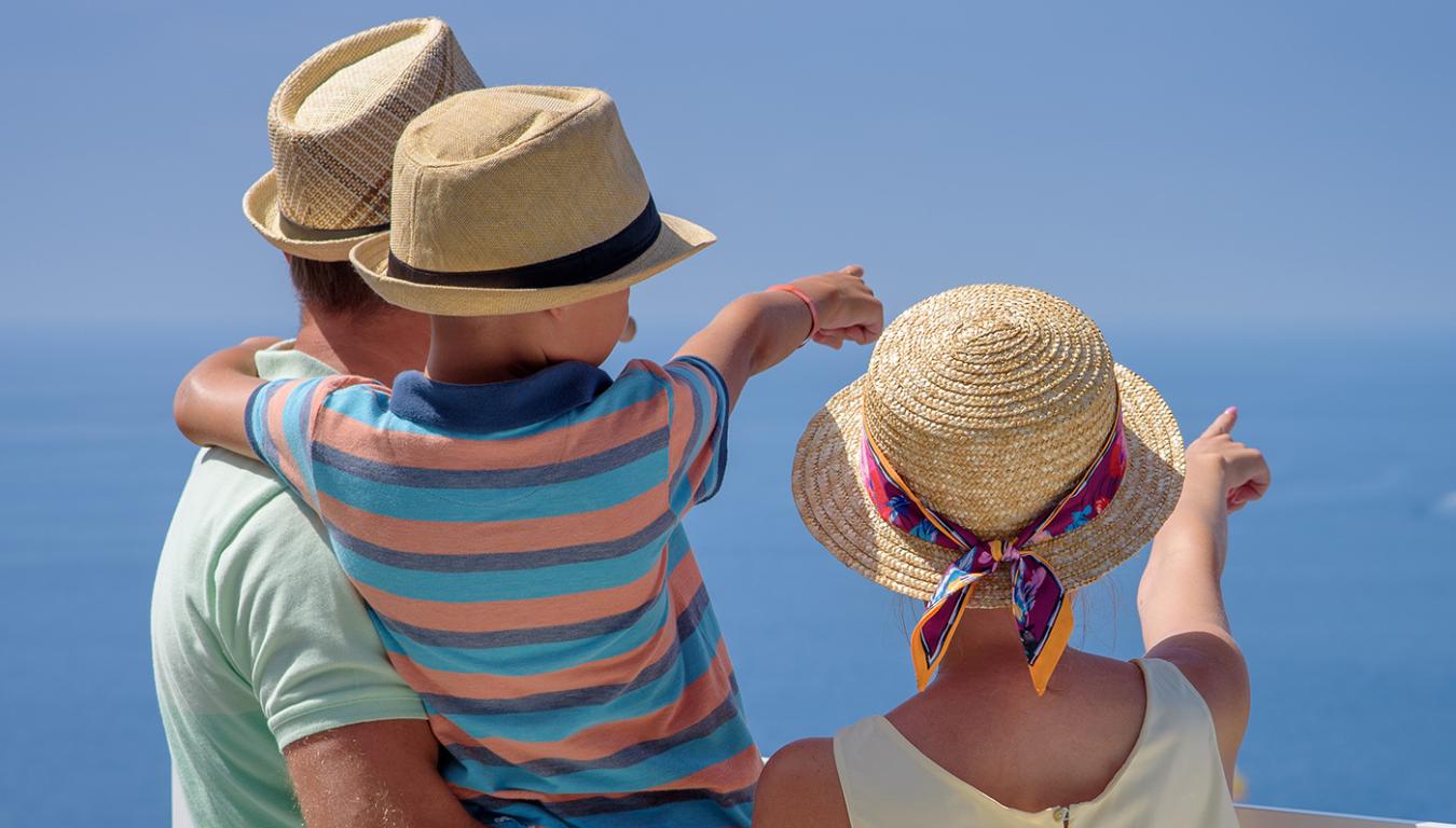 Famiglia guarda il mare, indossando cappelli di paglia, in una giornata soleggiata.