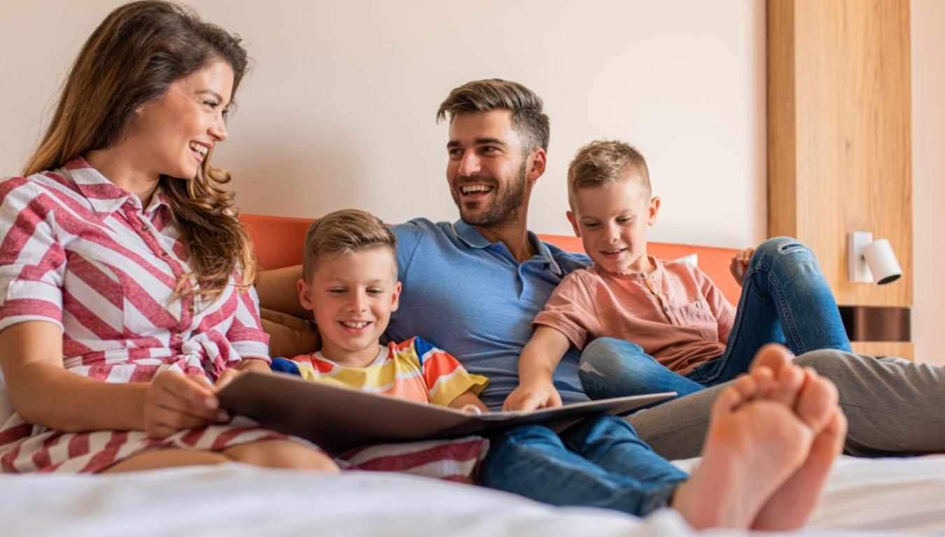 Famiglia felice seduta sul letto, leggendo insieme e sorridendo.