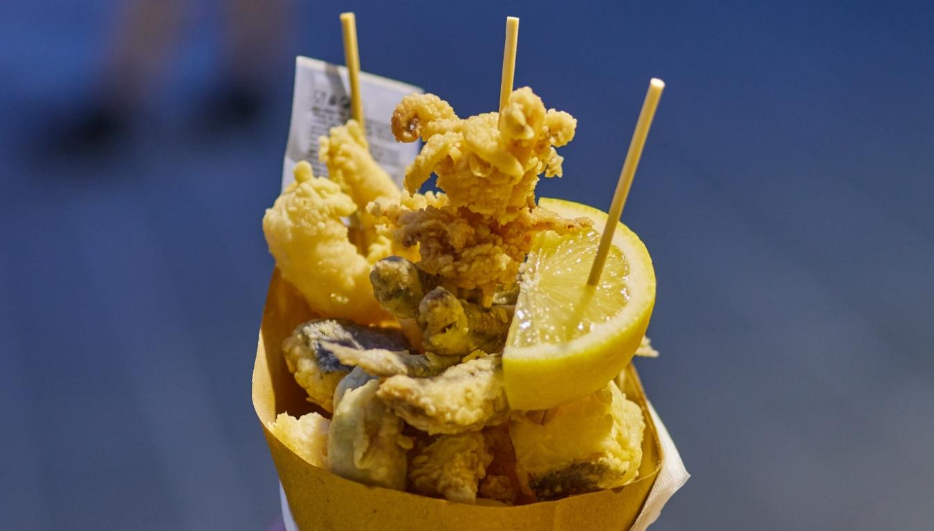 Cartoccio di fritto misto di pesce con limone, servito su spiedini.