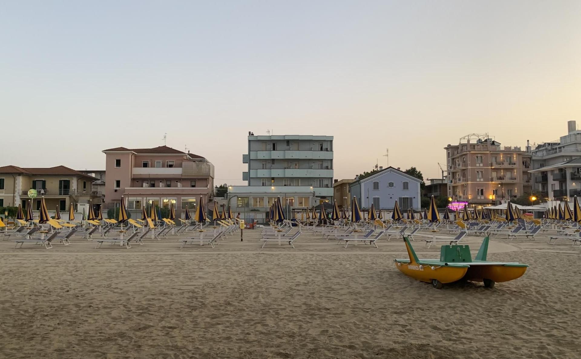 Spiaggia al tramonto con ombrelloni chiusi e pedalò sulla sabbia.