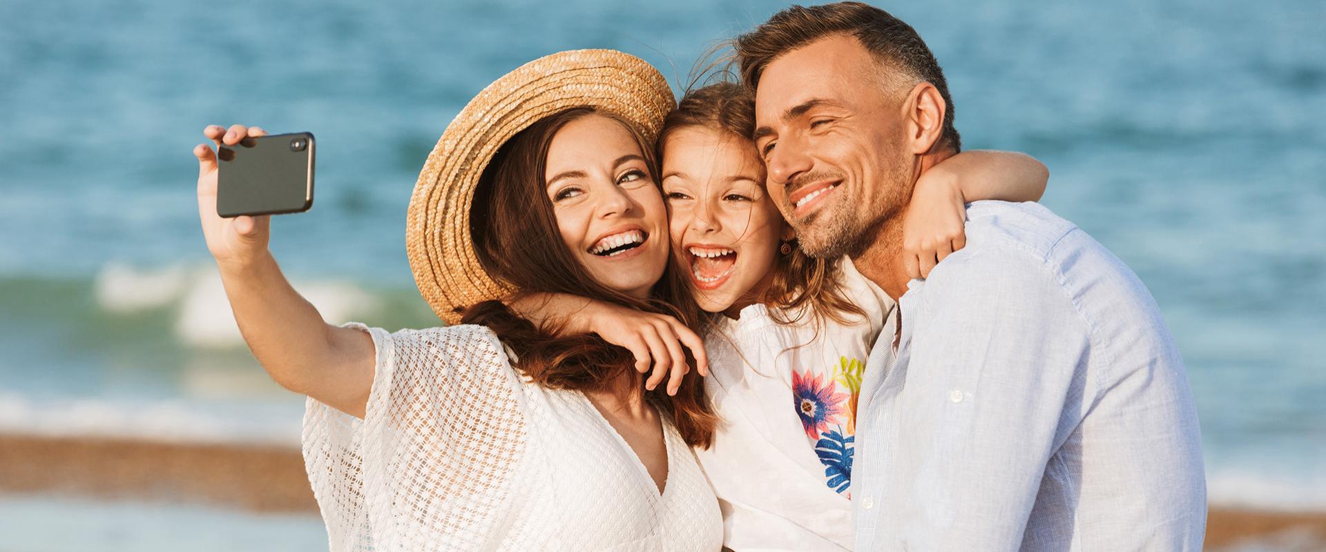 Famiglia felice scatta un selfie sulla spiaggia con il mare sullo sfondo.