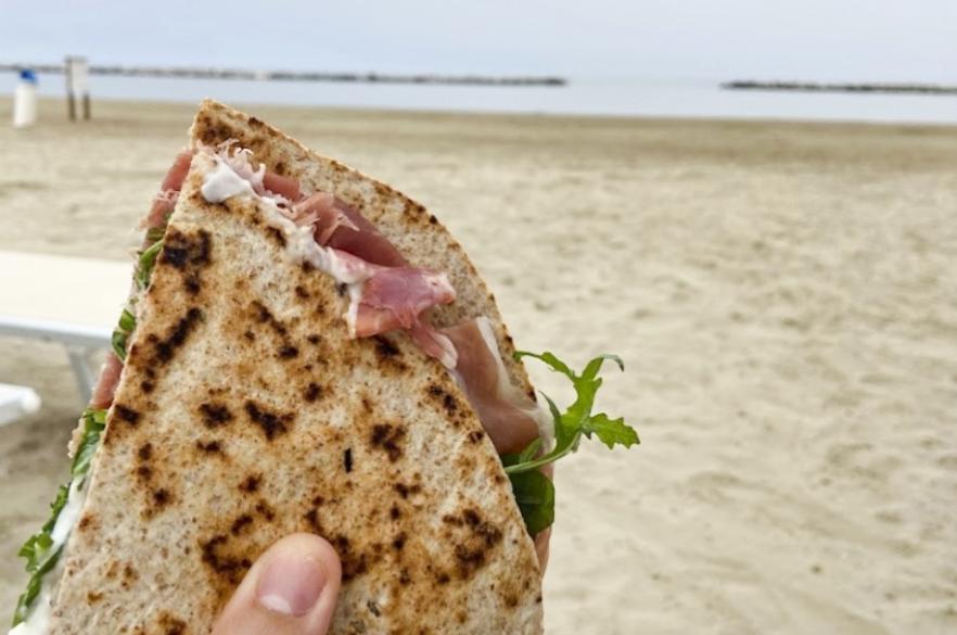 Piadina con prosciutto e rucola, gustata sulla spiaggia con vista mare.